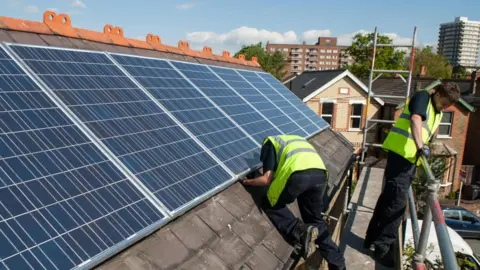 Elmbridge Borough Council Two men install solar panels on the roof of a house