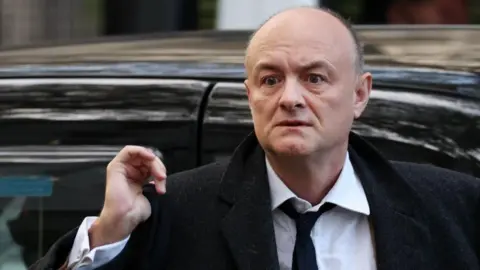 EPA Dominic Cummings, wearing a black coat, white shirt and black tie, exits a car
