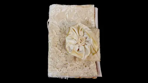 Oliwia Palika The picture shows a very delicate looking book made of fine wedding dress fabric including what looks like a silk rose.