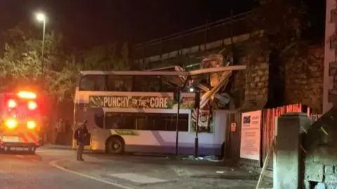 Chris Turner The top deck of a bus looks crushed by the impact of the crash into the railway bridge