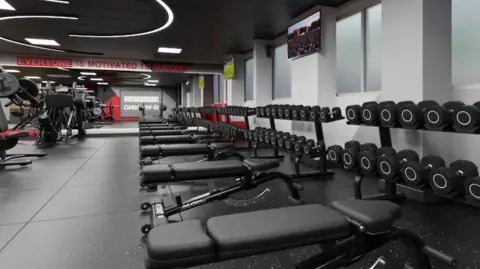 Everyone Active A large room with frosted windows. A row of weightlifting benches line the right hand wall, with weights on racks at the end of the benches.