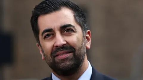 Getty Images Humza Yousaf, with dark hair and dark beard, in front of a blurred brown background 