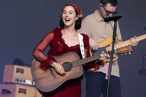 Getty Images Gracie Abrams plays a walnut-effect acoustic guitar during a concert in 2025