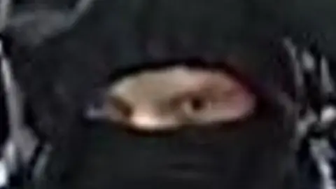 West Midlands Police The eyes of a person stare out from behind a black face covering