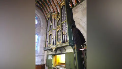 Bridget Weaving A 19th Century organ with green casing and gold and black pipework inside a stone Hanbury church.