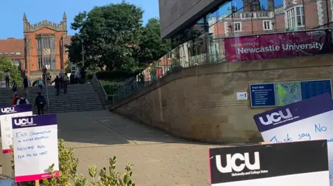 Matt Perry Newcastle University building in background with UCU picket line signs in foreground. One of the signs says "End casualisation in higher education".