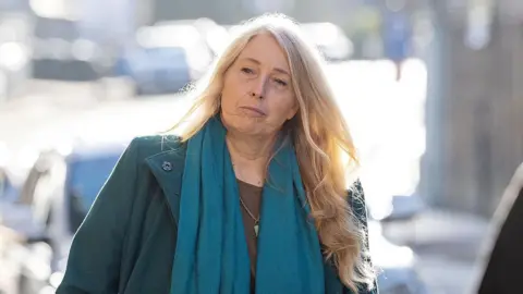 PA Media Sacha Dench is outdoors on a sunny day. She has long blonde hair and is wearing a green jacket and green scarf.