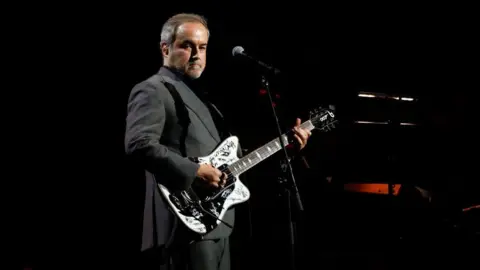Getty Images David Arnold playing a signed white electric guitar on stage