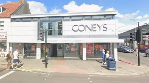 An image of a shop with a large sign saying Coneys on it, it's on the corner of a junction. 