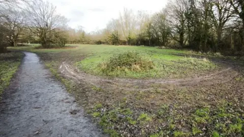 LDRS Park lawns with circular print of tyres on a mud trail around grass. Trees are dotted about.