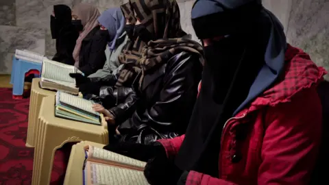 Women with their faces covered sit on the floor studying