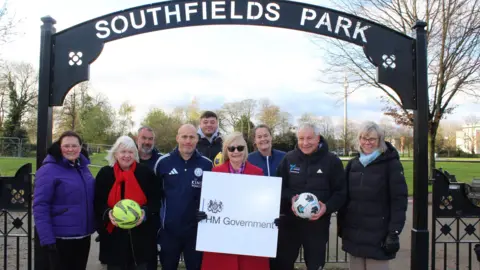 Charnwood Borough Council A group of people stood in front of a black iron arch which says Southfields Park on