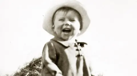 Hestercombe House Trust A small boy in a brimmed hat and an old-fashioned coat with a collar wears an expression of joy, with his mouth wide open