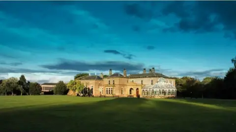 Preston Park Museum A large stone country manor sits in a expansive green lawn, surrounded by large trees.