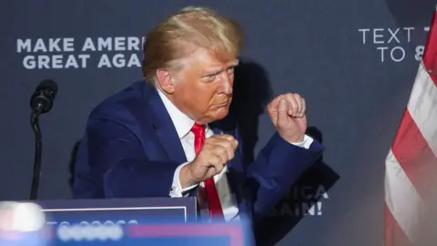 Donald Trump draagt ​​een blauw pak en een rode stropdas en danst terwijl hij het podium verlaat tijdens een campagnebijeenkomst in New Hampshire