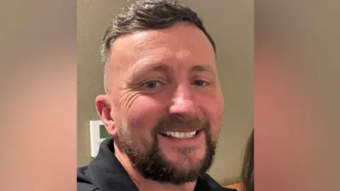 Nottinghamshire Police A man with short dark hair and a beard, smiling and wearing a black colllared jacket