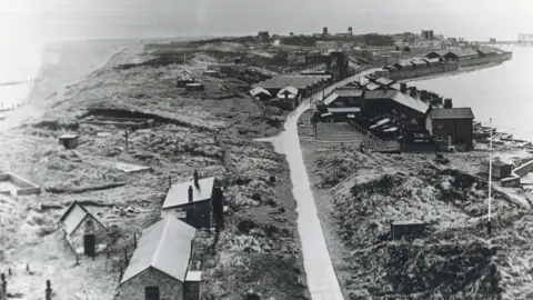 East Riding Archives and Local Studies A black and white photo of a peninsula surrounded by sea with a narrow road in the middle and houses to either side of it.
