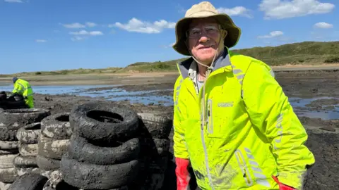 Andrew Stride, from Ogmore Angling Association wears a hi-vis jacket and is pictured next to tyres