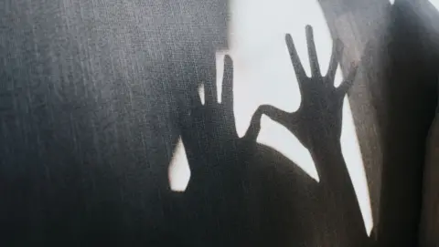 The shadow of a pair of hands against a white wall.