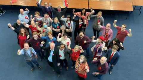 Nadia Gyane/BBC A group of people, wearing Labour rosettes, cheer and celebrate. The picture has been taken from above and they are all looking up at the camera.