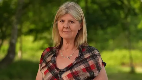 Martin Giles/BBC Alison Downes wearing a red and black top stood in front of some trees