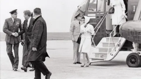 RAF Waddington Heritage Centre A black and white photograph showing President Kennedy on the RAF Waddington runway, shaking hands with a man in RAF uniform. Several women are in the background, disembarking from the US Sikorsky military helicopter following the trip to Derbyshire.