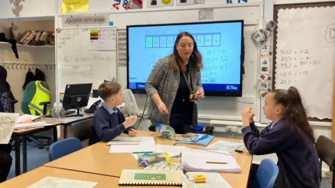 A teacher in a classroom supports two young children with their work