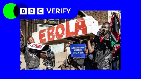 Protesters march during a demonstration against a controversial US-built Ebola quarantine centre. There is blue and green BBC Verify branding in the top left.