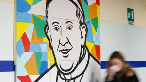 EPA The blurred figure of a woman dressed in black walks past a mural of Pope Francis, which consists of a line drawing of his head and shoulders set against a background of multi-coloured shapes.