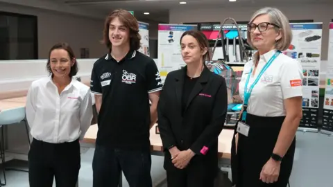 From left to right: Vanina Ickx, a representative of Oxford Brookes Racing, Marta Garcia and an event organiser posing for a picture at the International Women in Engineering Day event. They are looking away from the camera.
