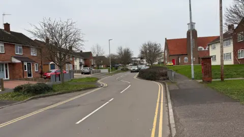 Two cars drive down the chicanes on Eastwick Road in Taunton with houses either side. It is a two-lane road with double yellow lines each side