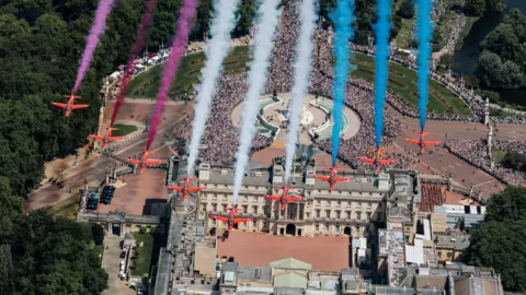 View from above as nine Red Arrows jets fly over Buckingham Palace trailing red, white and blue smoke behind them
