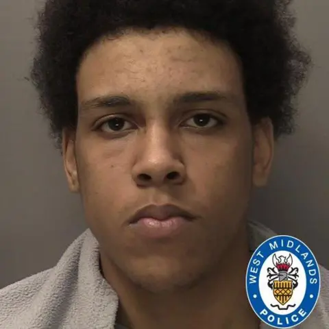 West Midlands Police Jovarn Esterine is seen in a police photograph, with the West Midlands Police logo in the corner. He is wearing a grey top and is looking straight at the camera.