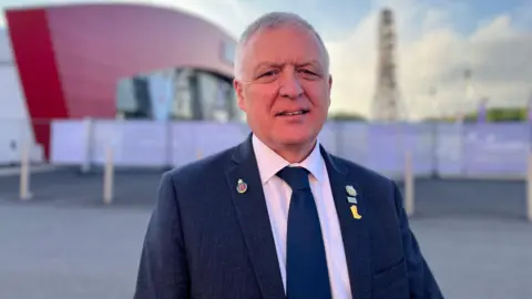 William Irvine wearing a navy suit, white shirt and navy tie.