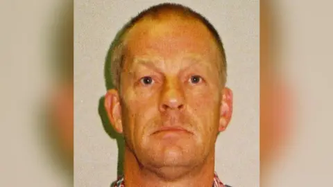 West Mercia Police Layton Davies mugshot. He is looking at the camera expressionless. He has very short grey hair.