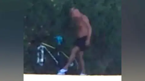 West Mercia Police A blurry CCTV image showing a topless man in black shorts standing next to a lime green coloured bike. 