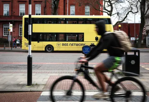 EPA-EFE/REX/Shutterstock A cyclist in the foreground rides past a yellow, bee network branded bus in the background.