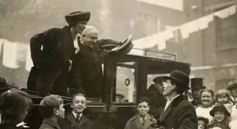 Plymouth Museums Archive A black and white photo of a woman standing on a car and addressing a crowd of people.
