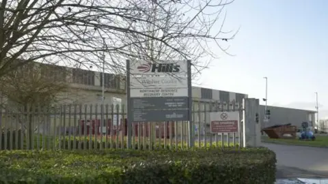The exterior of the Northacre Mechanical Biological Treatment plant. It is a large grey building with a grey metal fence around the exterior