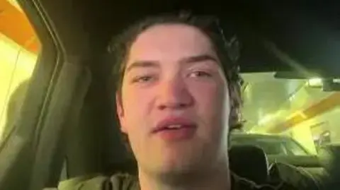 Handout A young man sat in a car looking to camera