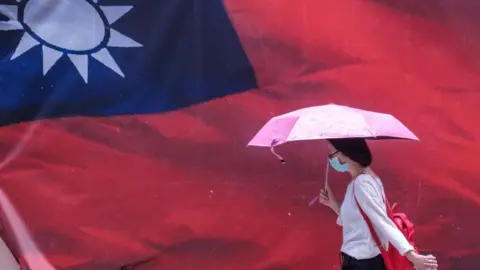 Getty Images A woman carrying an umbrella walking past a giant Taiwan flag