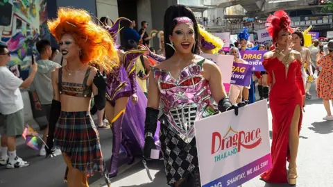 Getty Images Three drag queens parading on the street in Thailand, wearing colourful outfits
