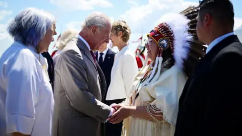 Reuters Britain's King Charles meets with an elder as he and Queen Camilla arrive at Ottawa Airport in Ontario, Canada, as the queen wears a pale pink fringed coat dress and a Maple leaf diamond brooch gifted to HMQ Elizabeth the Queen Mother by George VI, worn by QE2 for her first ever visit to Canada in 1939, May 26, 2025.