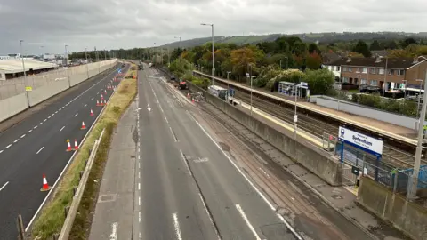 Pacemaker An empty Sydenham bypass in Belfast, lined with traffic cones during a weekend closure for resurfacing.  The sign for Sydenham train station and the train tracks can be seen at the right of the photo.