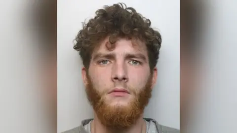 Northamptonshire Police A police mugshot of Joshua Coulton, who has curly red hair and a thick beard.