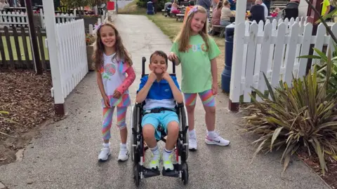 Karen Stirrat A boy in a wheelchair with two young girls beside him, outside a circus