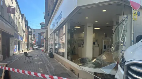 A badly damaged shopfront with a large pane of smashed glass having been removed from the building.