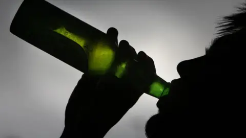 A man in silhouette drinks from a beer bottle 