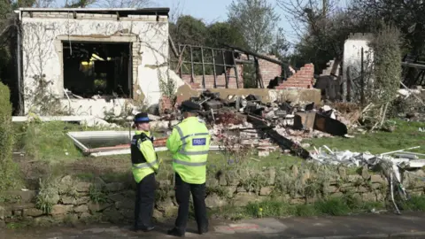 BBC Police view debris in a rural garden after the blast