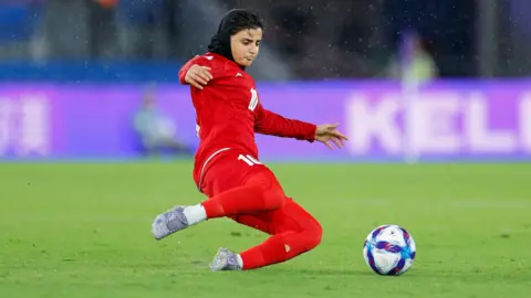A woman in a red uniform dives to get a ball
